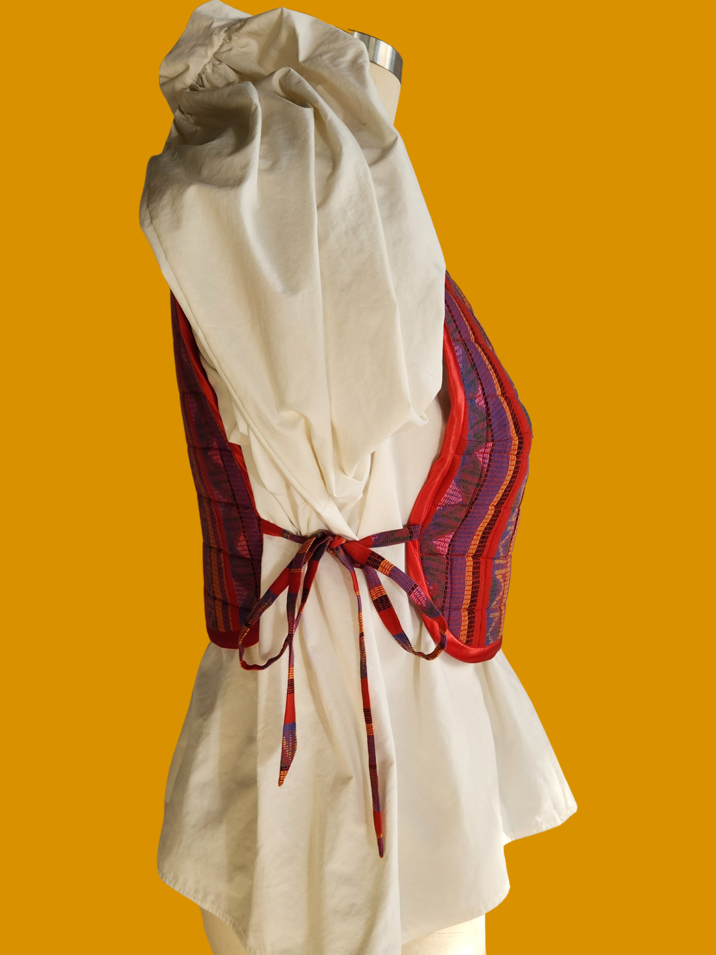White dress with a red and purple patterned sash on an orange background
