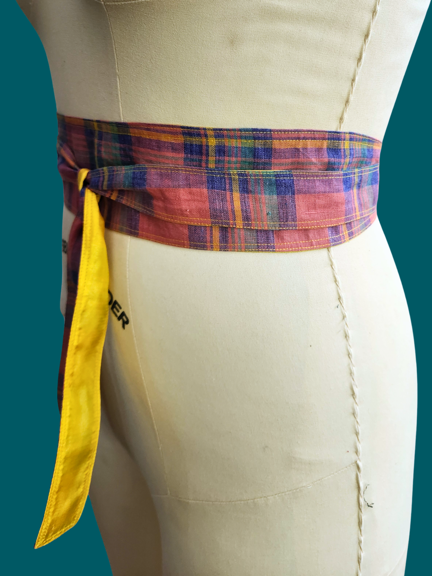 Colorful plaid belt with a yellow tie on a mannequin against a teal background