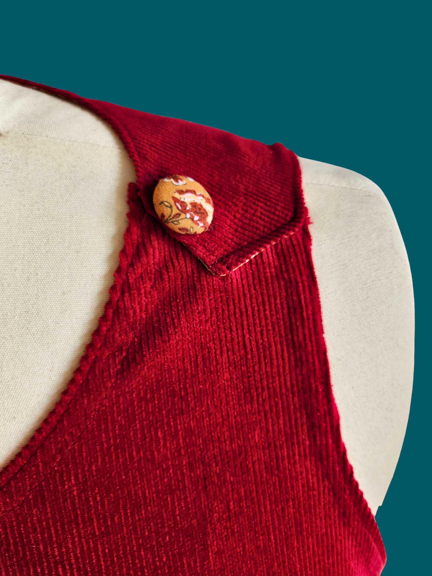 Red knitted vest with a button on a mannequin against a teal background