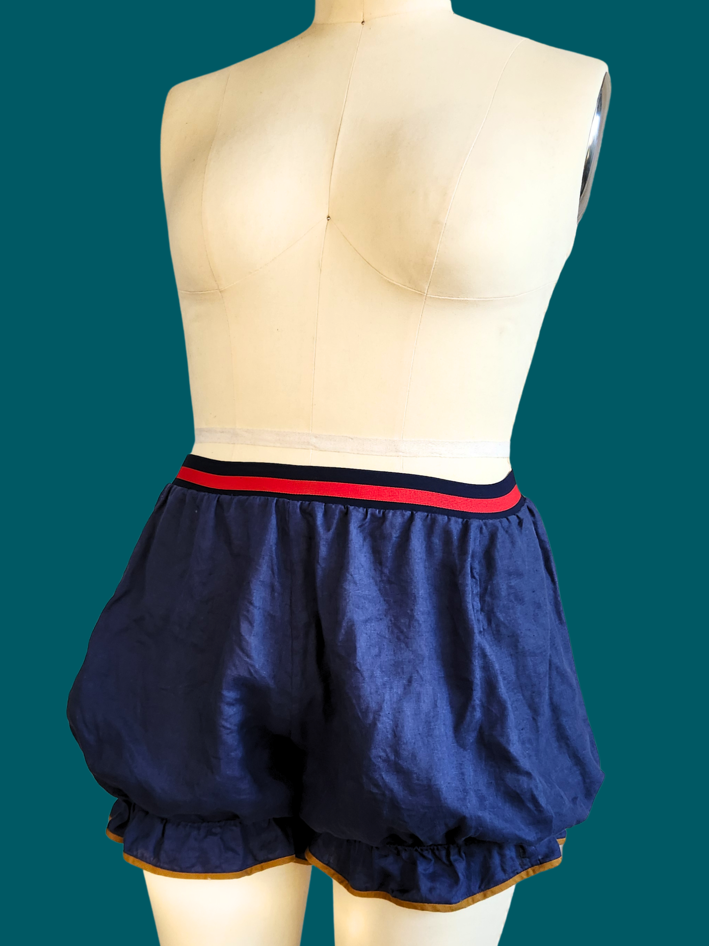Navy blue shorts with a red waistband on a mannequin against a teal background
