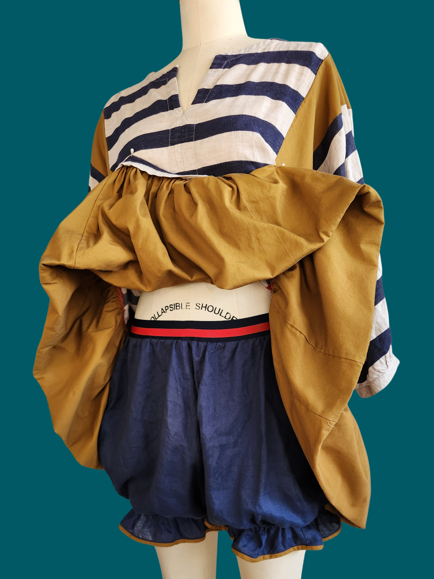 Mannequin wearing a striped shirt, mustard jacket, and navy shorts on a teal background