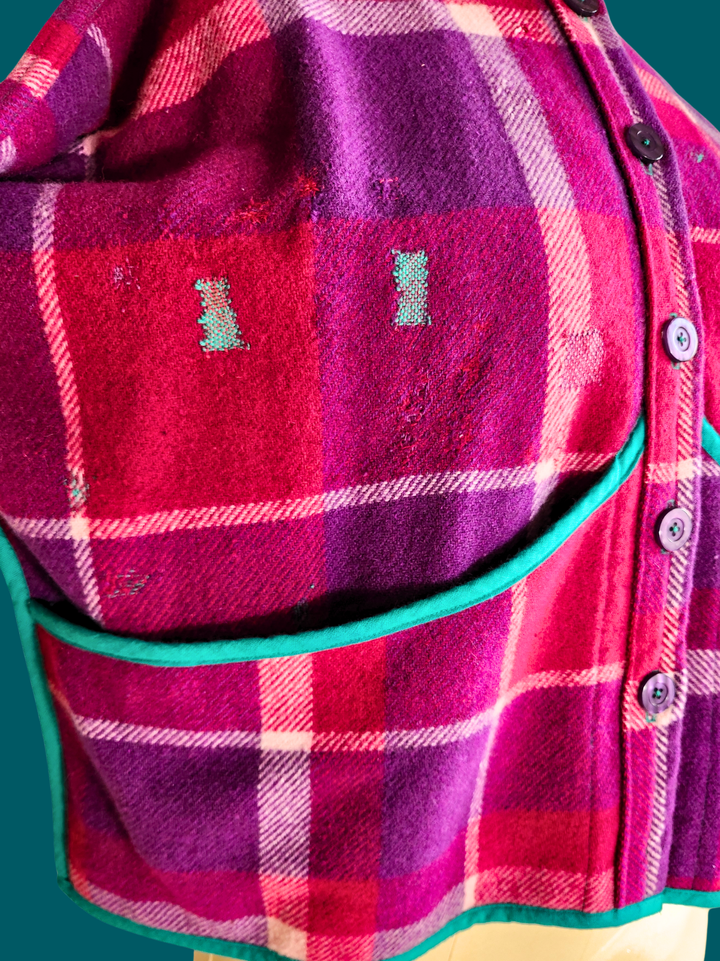 visible mending on front of pink plaid jacket on teal background