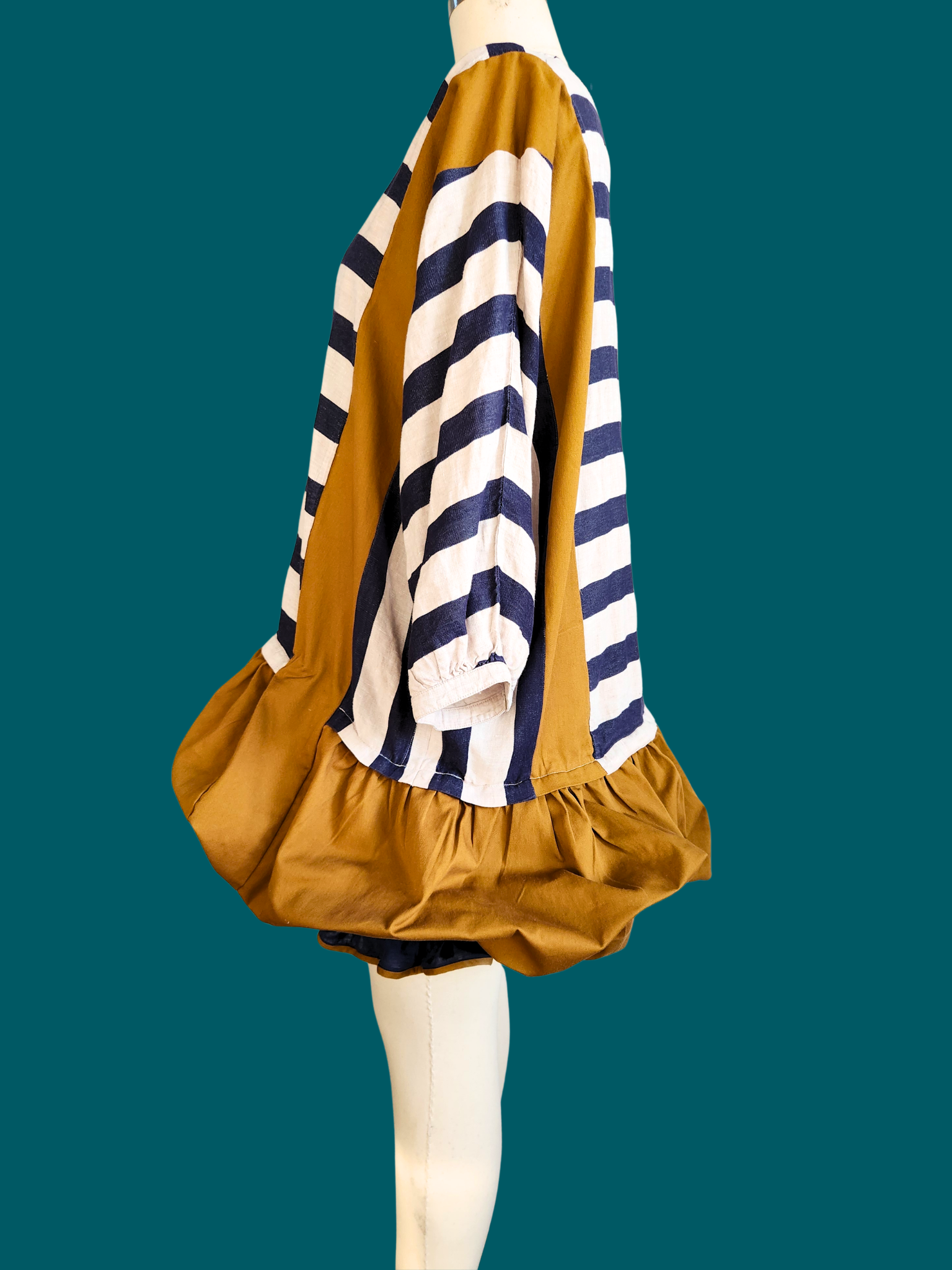 Mannequin wearing a mustard yellow dress with a navy and white striped top on a teal background