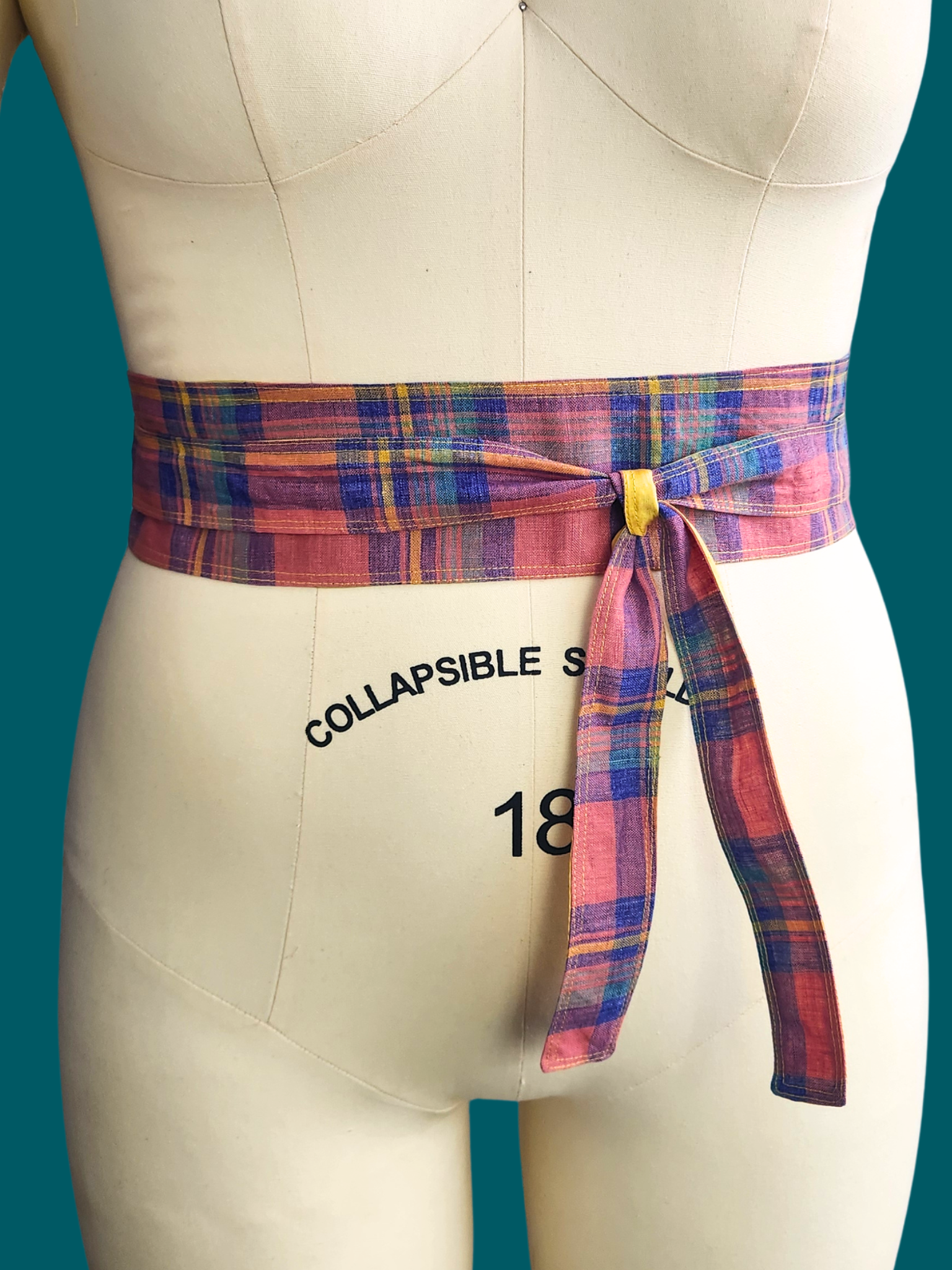 Mannequin wearing a plaid belt with 'Collapsible S' text on a teal background