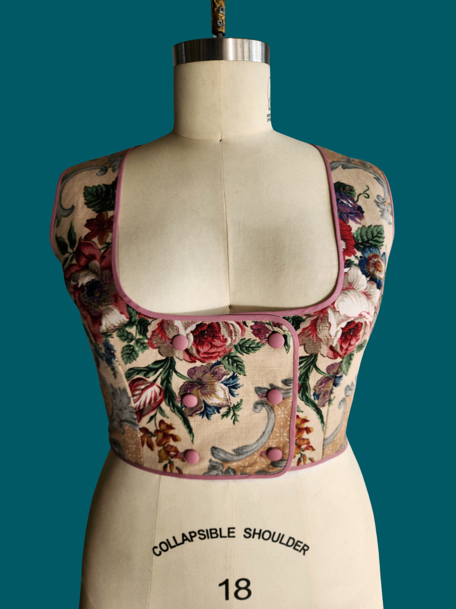 Floral embroidered top on a mannequin with 'Collapsible Shoulder' label against a teal background