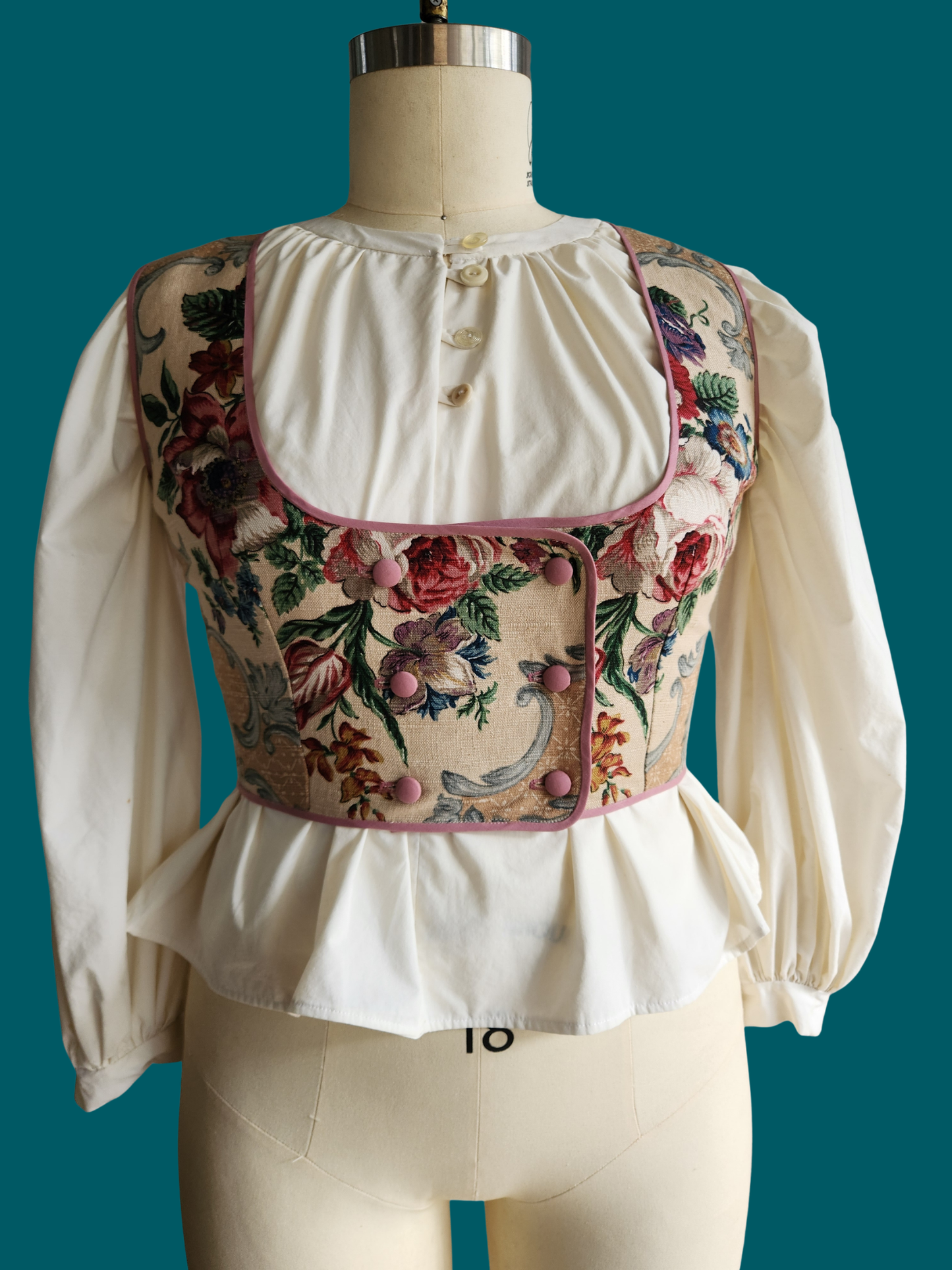 Vintage-style blouse with floral embroidery on a mannequin against a teal background