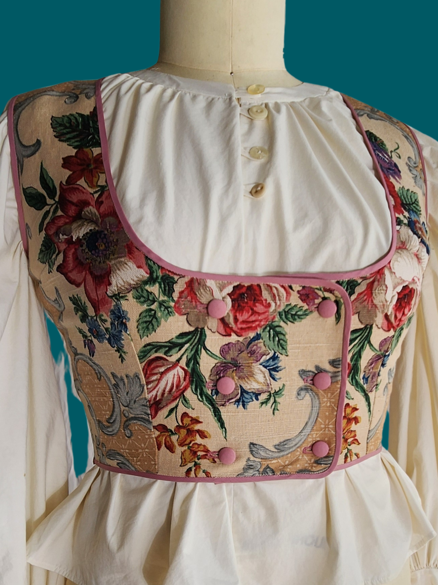 Floral embroidered vest on a mannequin against a teal background