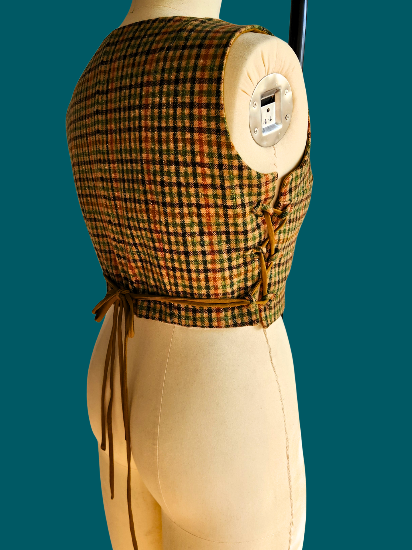 Mannequin wearing a plaid top and beige pants against a teal background
