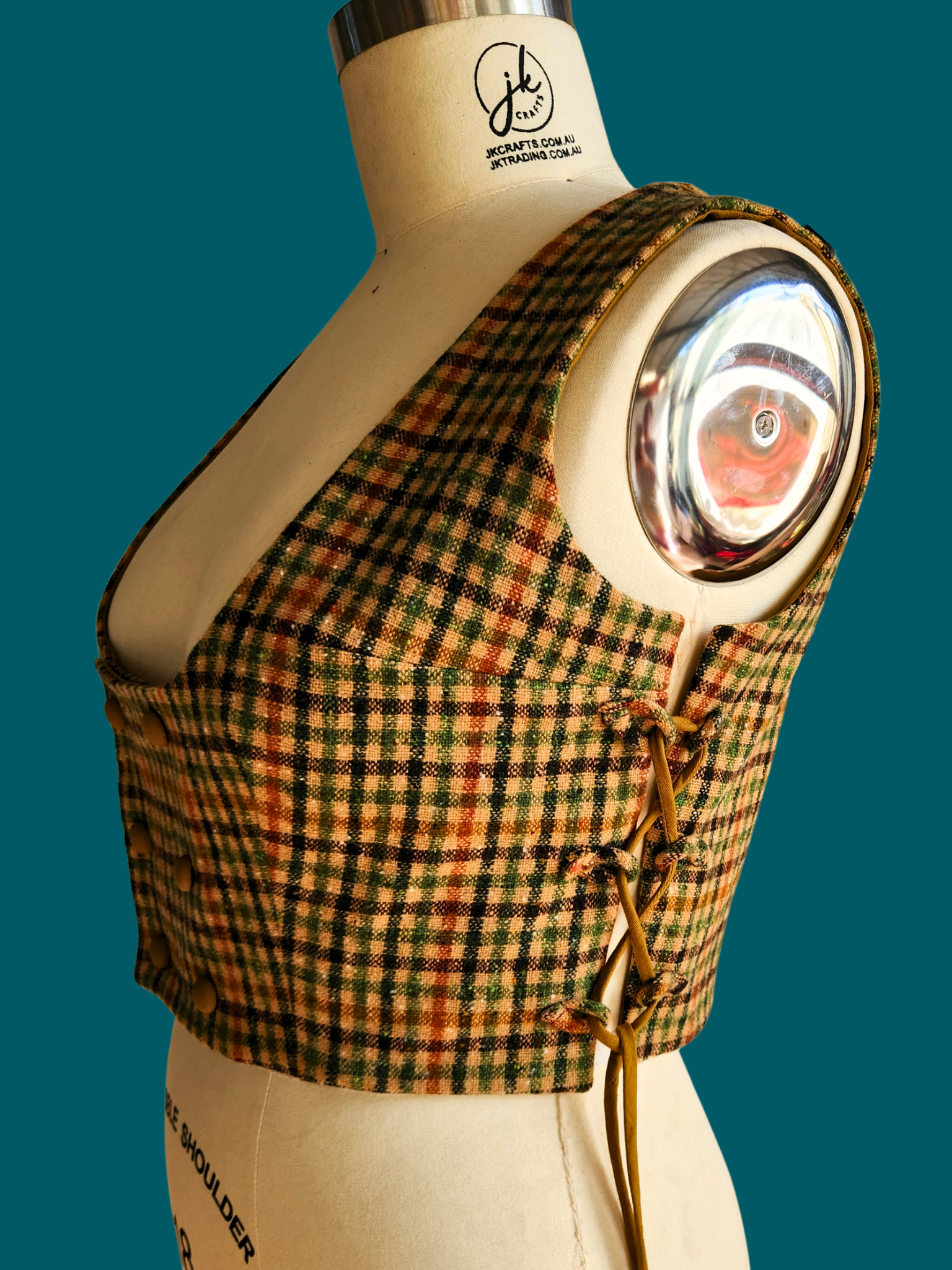 Plaid garment with a circular design on a mannequin against a teal background
