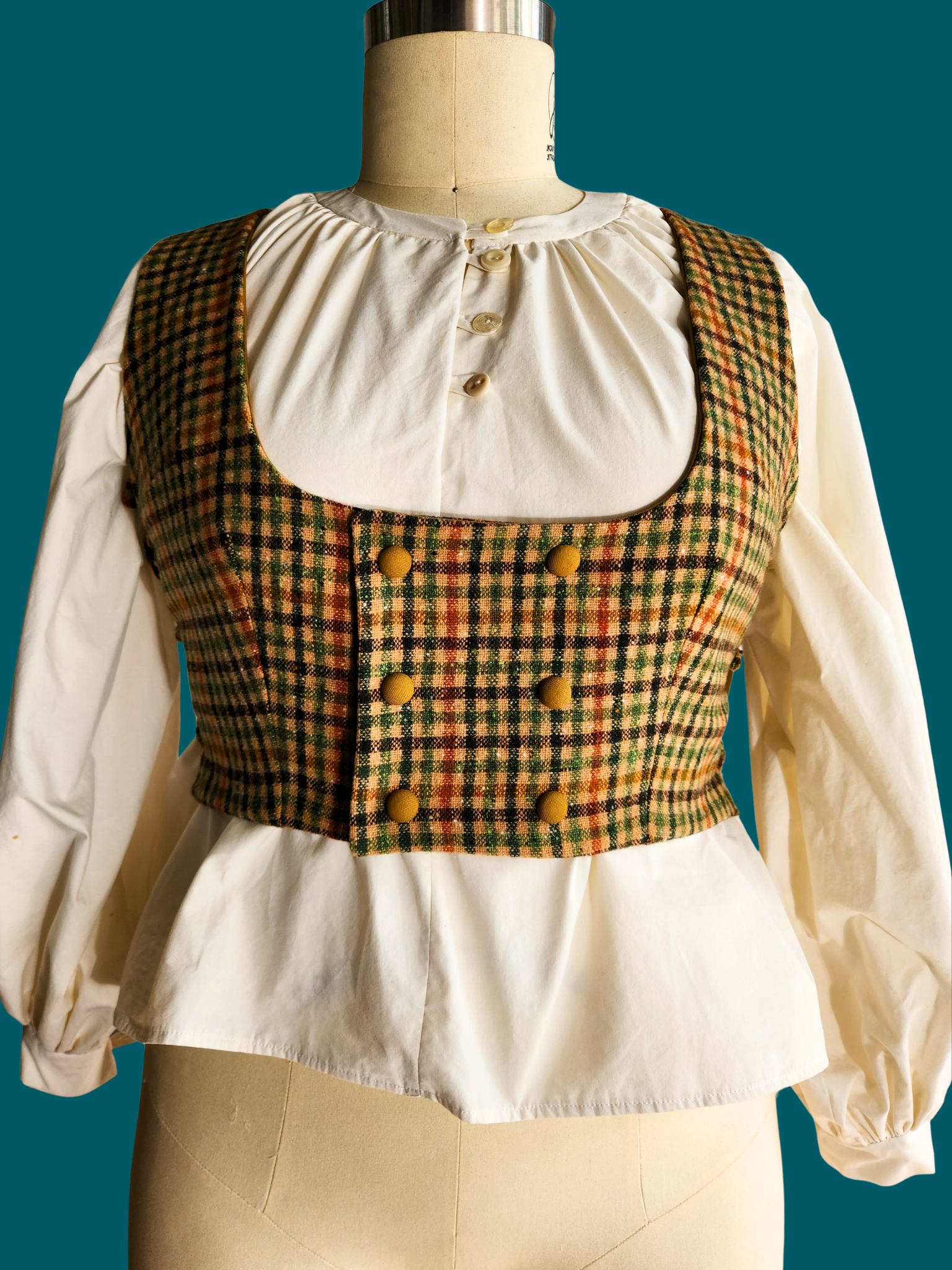 Mannequin wearing a white blouse with a plaid vest against a teal background