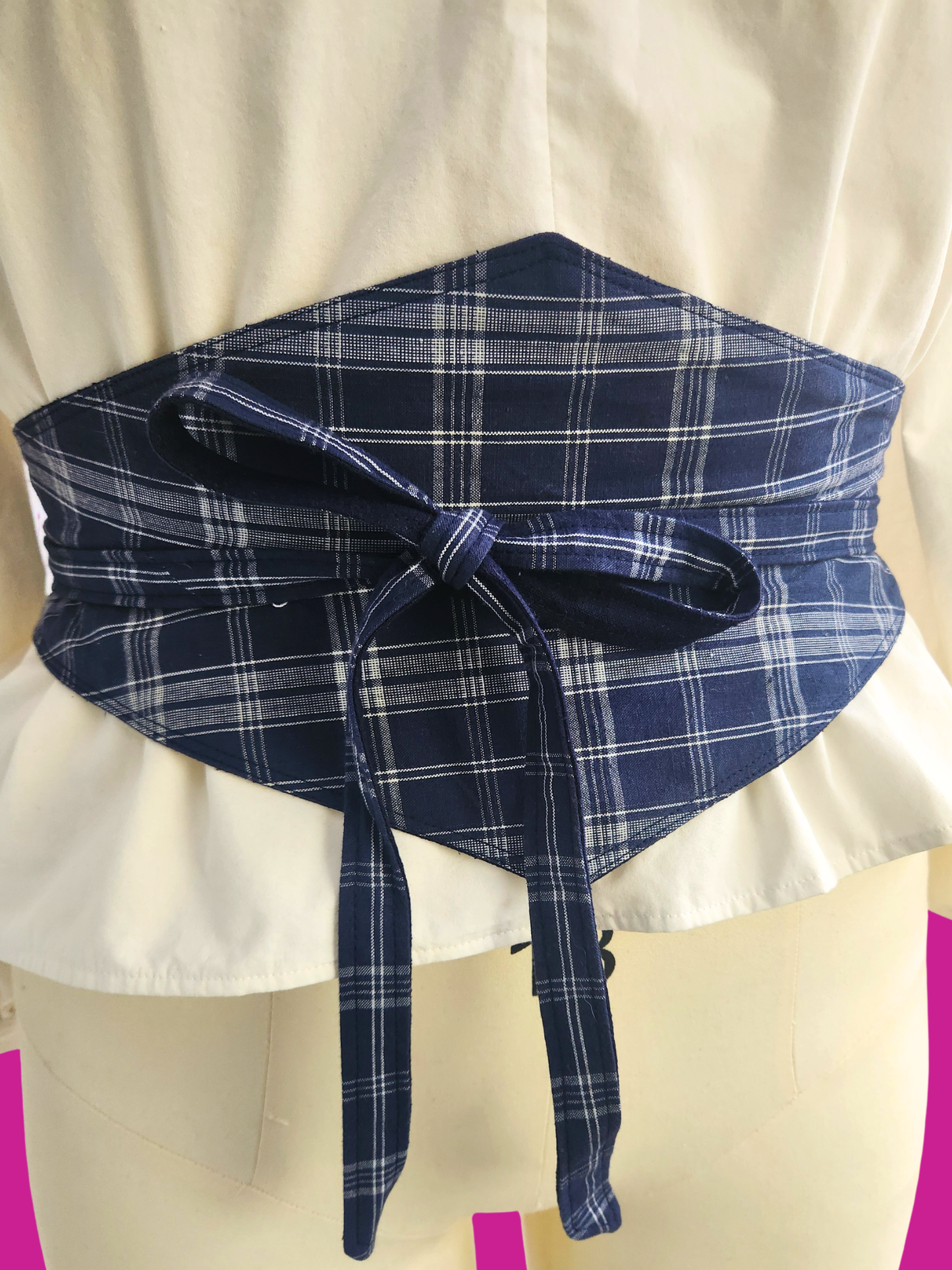 Blue plaid sash tied around a white garment on a mannequin.