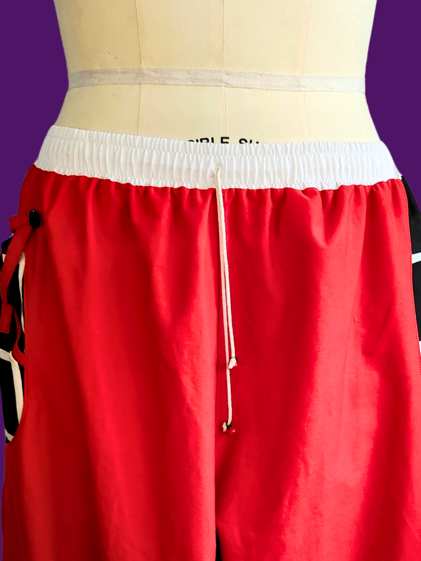 Red shorts with a white waistband on a mannequin against a purple background