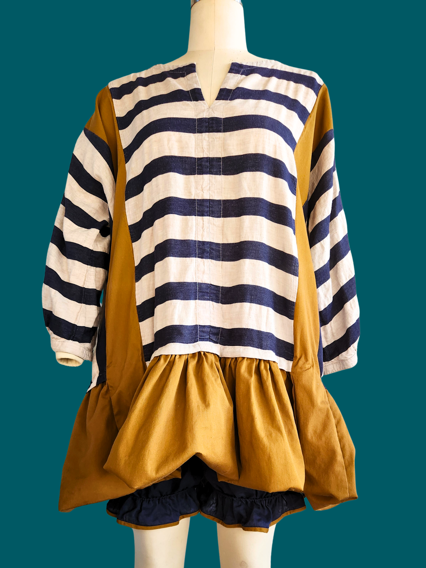 Mannequin wearing a striped shirt and mustard yellow dress against a teal background