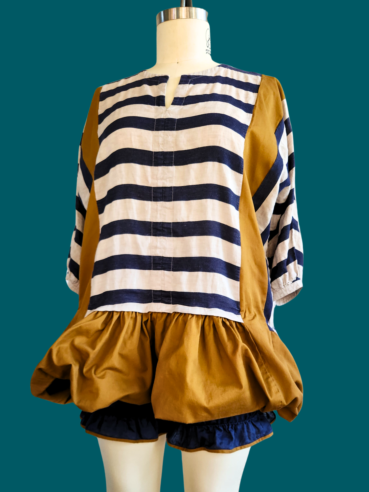Mannequin wearing a striped shirt and mustard-colored shorts with ruffles on a teal background