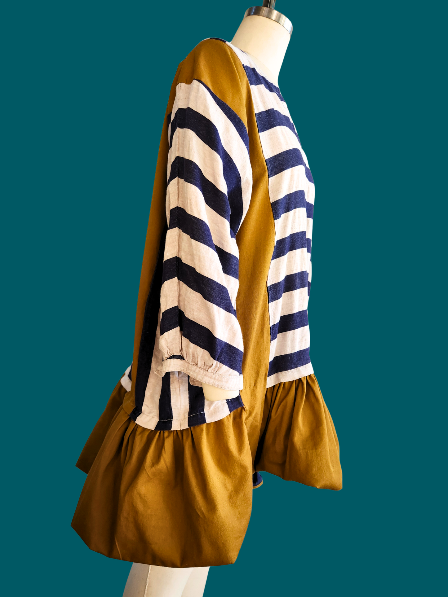 Mannequin wearing a mustard yellow dress with a blue and white striped top on a teal background